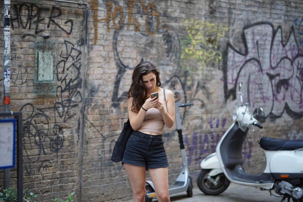 woman in black shorts and black brassiere standing beside white motor scooter during daytime